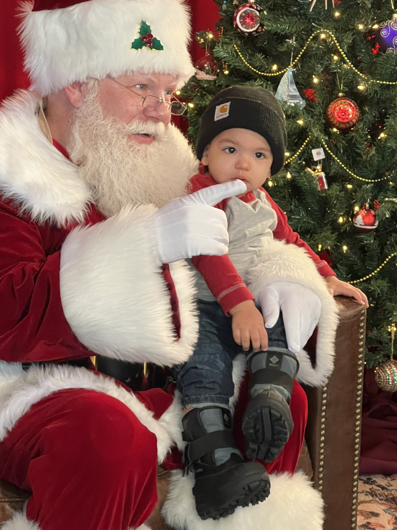 Santa holding a baby in front of a Christmas tree