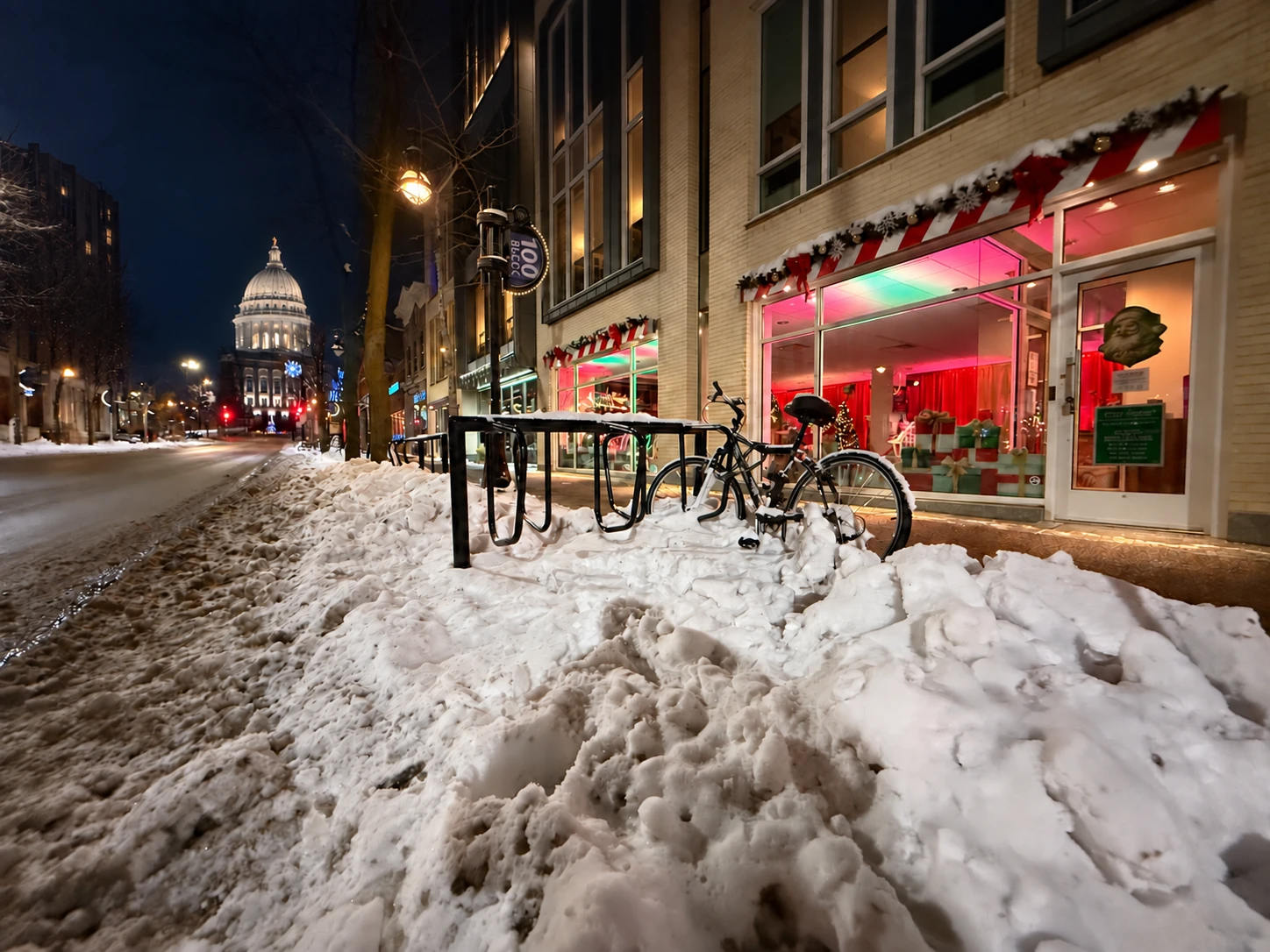Snowy winter evening on State Street with the Wisconsin State Capitol in the distance and the Santa on State storefront glowing at right