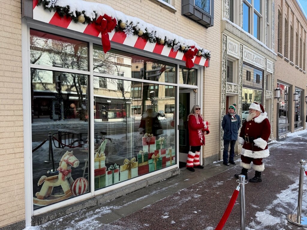 Santa greeting visitors outside the decorated storefront on State Street in the snow